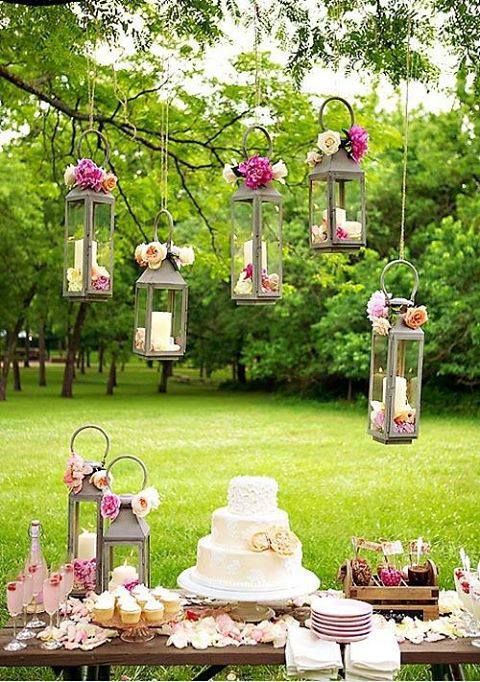 wesele w stylu rustykalnym i dekoracje stołu w tym stylu - lampiony podwieszane i stół ustawiony na świeżym powietrzu udekorowany stroikami z kwiatów w kolorze różu i kremu