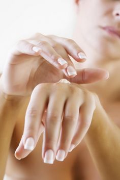 domowe manicure - na pierwszym planie piękne i zadbane dłonie z pięknymi paznokciami na które młoda kobieta nakłada krem